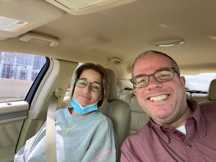 Tara and Chuck in the car after surgery. Tara with a mask pulled down to her chin.